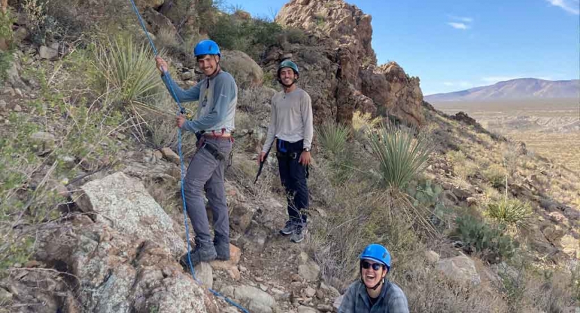 a group of gap year students smile while belaying rock climbers on an outward bound expedition 